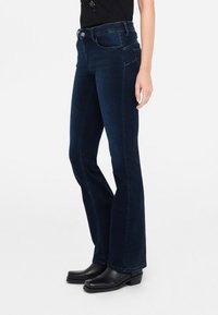 Jeans a zampa d'elefante in denim blu scuro, con un classico design a cinque tasche, cuciture a contrasto e chiusura con bottone adornata da un accento metallico decorativo.