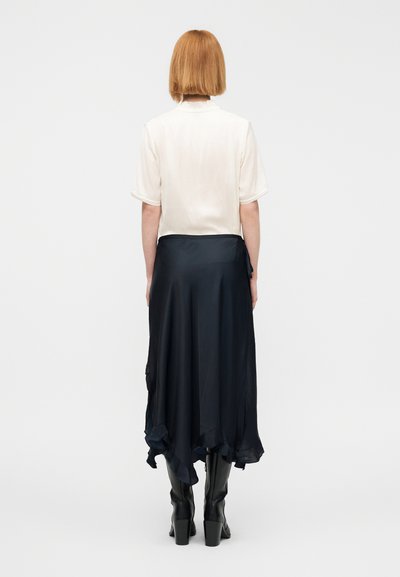 Μπλούζα από μεταξωτή κρέπα συνδυασμένη με μια αέρινη μπλε φούστα με βολάν στο τελείωμα και μαύρες μπότες έως το γόνατο με χοντρό τακούνι.