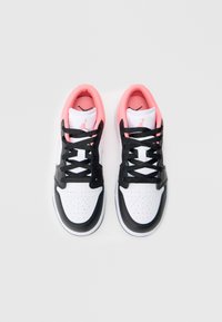 Balti ir juodi sportiniai batai su rožiniu vidumi, turintys juodas raišteles, perforuotus akcentus ant piršto ir ikonišką prekinį ženklą ant liežuvio.