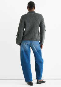 Maglione grigio lavorato a maglia con collo alto, vestibilità ampia e maniche a sbuffo testurizzate, abbinato a jeans in denim blu a gamba larga e ballerine nere.