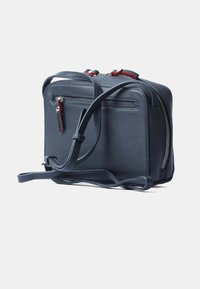 Borsa a tracolla in pelle blu navy con due tasche con zip, tracolla regolabile e dettagli rossi, caratterizzata da una texture liscia e forma rettangolare.