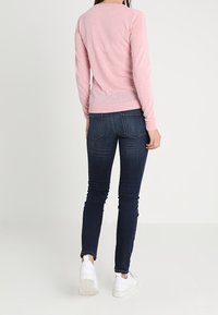 Haut rose à manches longues avec un col rond, porté avec un jean skinny en denim foncé et des baskets blanches, vu de dos.