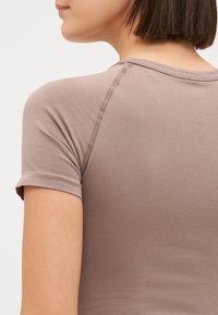Fitted, short-sleeve t-shirt in soft, brown fabric. Features a round neckline and visible stitching along the shoulder seam.