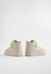Baskets montantes beiges en cuir lisse, avec un design cousu, une pointe arrondie et des bandes Velcro pour un maintien sécurisé.