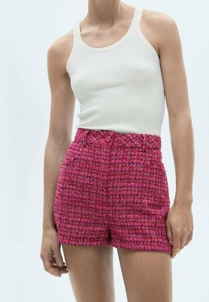 Femme portant un débardeur blanc côtelé et un short rose texturé taille haute, debout devant un fond uni.