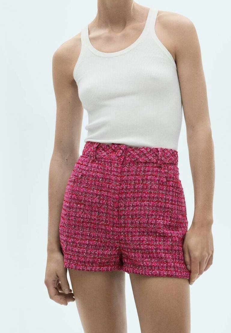Femme portant un débardeur blanc côtelé et un short rose texturé taille haute, debout devant un fond uni.