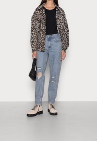 Bunda z umělé kožešiny s leopardím vzorem, černý top, světle modré džíny s trhaným efektem, krémové šněrovací boty s černými podrážkami a černá pletená kabelka.