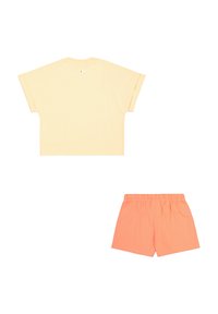 Camiseta de algodón en un suave amarillo con mangas anchas y un escote redondeado; combinada con pantalones cortos de algodón naranja que cuentan con una cintura elástica.