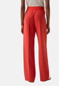 Czerwone spodnie o szerokich nogawkach wykonane z gładkiej tkaniny, z wysokim elastycznym pasem i przednimi zakładkami dla dodatkowego efektu.