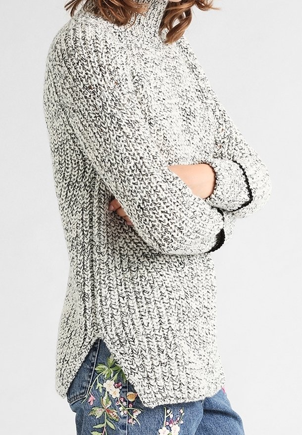 Chunky stickad tröja i grått och vitt med hög krage, sidofickor och svarta detaljer. Mjuk textur med avslappnad passform.