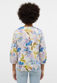 Blumenbluse mit blauen und lila Blumen auf hellem Hintergrund, mit rundem Ausschnitt und dreiviertellangen Puffärmeln.