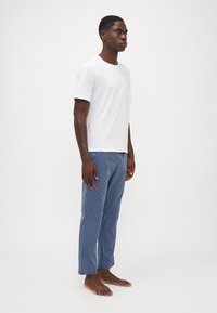 Hvid T-shirt med korte ærmer kombineret med blå og hvide stribede pyjamabukser. Bukserne har en afslappet pasform og lige ben-design.