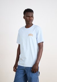 Világoskék pamut póló rövid ujjakkal, bal mellen narancssárga "DICKIES" logóval. Simább tapintású, lazább szabású.