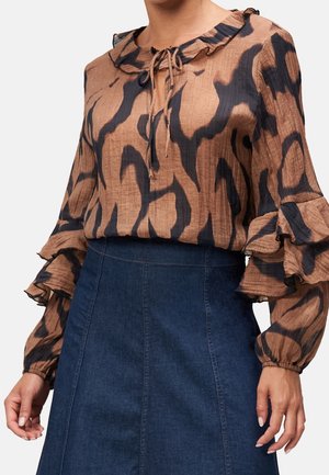 Brązowa i czarna bluzka w wzory z falbanianym kołnierzem i warstwowymi rękawami, zestawiona z ciemnoniebieską, wysokoprofilowaną spódnicą dżinsową.