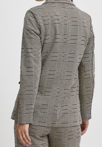 Grå och svart rutig kavaj med skräddarsydd passform, strukturerade axlar och en mjuk tygtextur, med slagkrage och ryggslits.