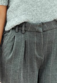 Grijze, gestructureerde wolmix trui met korte mouwen, gecombineerd met grijze pinstripe broeken met plooien en riemlussen.
