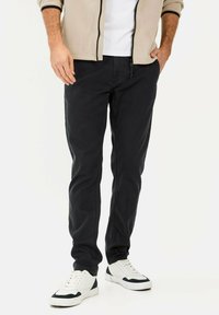 Sorte bomuldsbukser med lige pasform, parret med en beige fleecejakke med lynlås og hvide sneakers. Enkel design og tekstureret stof.