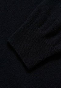 Tissu de pull en tricot noir montrant une manchette côtelée, une texture lisse et un motif de tissage uniforme. Aucun motif ou matériel visible.