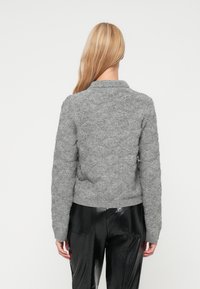 Γκρι πλεκτό πουλόβερ με υφή, ραμμένες μανσέτες και στρίφωμα, καθώς και γιακά. Φορεμένο πάνω από μαύρο δερμάτινο παντελόνι, προοπτική από την πλάτη.