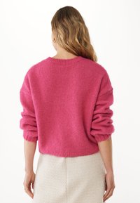 Puszysty różowy sweter o skróconym kroju, luźnych rękawach i prążkowanym dekolcie. Noszony z teksturowaną białą spódnicą, pokazujący widok z tylu.