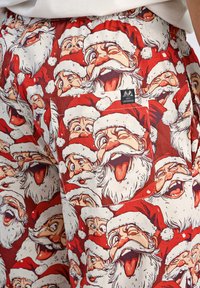 Rode shorts met een herhalend patroon van cartoon Santa gezichten met witte baarden en rode hoeden. Inclusief een achterzak met een merketiket.
