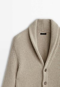 Beige knitted cardigan with a shawl collar, featuring a ribbed texture and two brown button closures at the front.