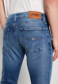 Blå denimjeans med slim fit, som har en brun läderetikett bak, två bakfickor och subtil utblekning på tyget.