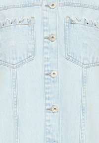 Veste en denim bleu clair vue de face avec deux poches poitrine ornées de dentelle œillet blanche et boutons argentés le long du centre.
