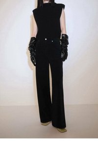 Modèle portant un haut en tricot noir sans manches, un pantalon large noir taille haute, de longs gants en cuir noir et des chaussures beige à bout carré.