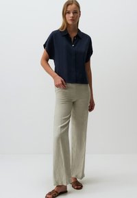 Camicia a maniche corte di colore navy, di vestibilità ampia, abbinata a pantaloni a gamba larga beige chiaro realizzati in un tessuto testurizzato, completata da sandali marroni.