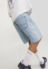 Ljusblå denimshorts med avslappnad passform, med bakfickor och gula sömmar, parat med vita strumpor och marinblå sneakers.