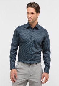 Camicia a maniche lunghe blu a fantasia con una vestibilità slim, caratterizzata da piccoli punti bianchi e colletto classico, abbinata a pantaloni grigi chiari.