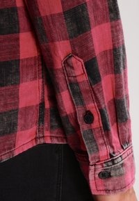 Rood en zwart geruite flanellen shirt met knoopmanchetten, voorzien van een zachte textuur en contrasterende zwarte knopen op de mouwen.