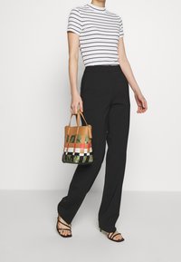 Top a rayas blanco y negro, pantalones negros y un bolso a cuadros colorido en tonos de verde, rojo y marrón. Sandalias negras con tiras.