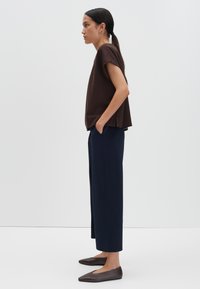 Bruine top met korte mouwen, marineblauwe broek met wijde pijpen en bruine platte schoenen. De stof lijkt glad en het ontwerp is minimalistisch met een relaxte pasvorm.
