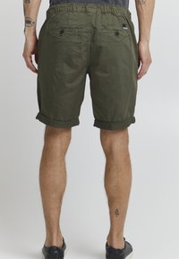 Shorts vert olive en tissu léger, avec un ourlet roulé, une taille élastique et deux poches arrière avec fermetures à bouton.