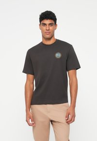 Juodas medvilnės marškinėliai trumpomis rankovėmis ir apykakle, su apvaliu "Tennis Heritage" logotipu žalia, geltona ir mėlyna spalvomis ant krūtinės.