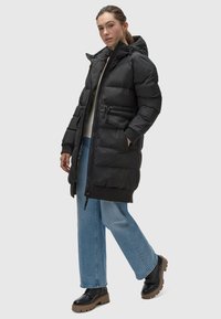 Black puffer coat with a hood, zip closure, and elastic cuffs. Features two front pockets, a cinched waist, and a longer length.
