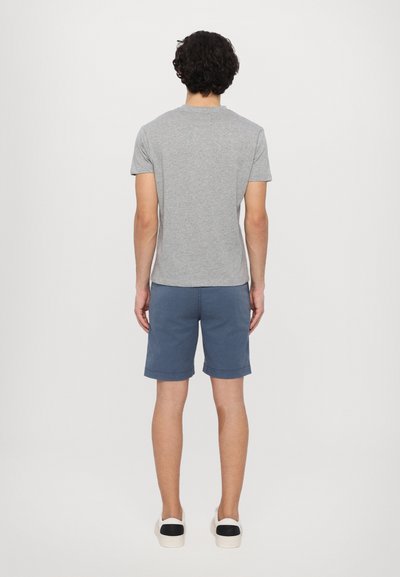 Camiseta de algodón gris de manga corta, combinada con pantalones cortos azules. Los pantalones cortos tienen dobladillos enrollados, y el conjunto se completa con zapatillas blancas.