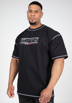 Camiseta de algodón negra con el texto "GORILLA WEAR" en blanco y rojo. Costuras de contraste en el cuello y las mangas. Diseño de corte holgado.