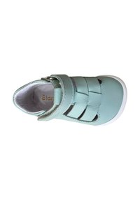 Zapato de cuero color aguamarina con una textura suave, punta cerrada, correa ajustable y detalles perforados para ventilación. Suela de goma blanca.