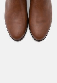 Bottines en cuir marron, avec une texture lisse, un bout arrondi et une semelle en caoutchouc noir, vues d'en haut. Design minimaliste, sans quincaillerie visible.