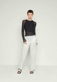 Black sheer long-sleeve top with sparkly details, paired with high-waisted, shiny silver wide-leg pants and black sandals.