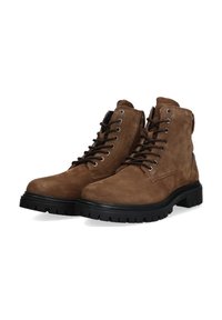 Botas de ante marrón hasta el tobillo con suelas de goma negra, que presentan ojales de metal y cordones negros. El diseño incluye un collarín acolchado para mayor comodidad.
