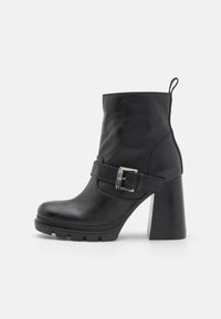 Botines negros de material sintético con tacón grueso, detalles de correa y hebilla, y suela texturada.