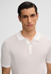 Polo bianco a maniche corte con finitura testurizzata, colletto classico e due bottoni sullo scollo. Tessuto morbido con un design aderente.
