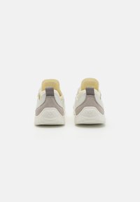 Scarpe sportive bianche e gialle con accenti in suede grigio, caratterizzate da un design slip-on e una suola in gomma testurizzata. Vista posteriore con branding minimale.