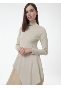 Beige coltrui gemaakt van zachte stof met lange mouwen, een asymmetrische zoom en een gladde textuur, met een aansluitende buste die uitloopt bij de taille.