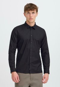 Black long-sleeve button-up shirt with a classic collar, featuring a smooth texture and subtle sheen, worn with gray trousers.