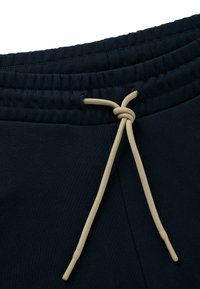 Pantaloni sportivi blu navy con cintura elastica e coulisse beige. Presentano una semplice texture di tessuto liscia e cuciture rinforzate.